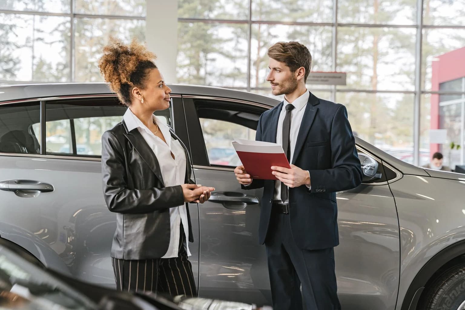 A woman discussing car purchase with a dealer inside a car dealership showroom.