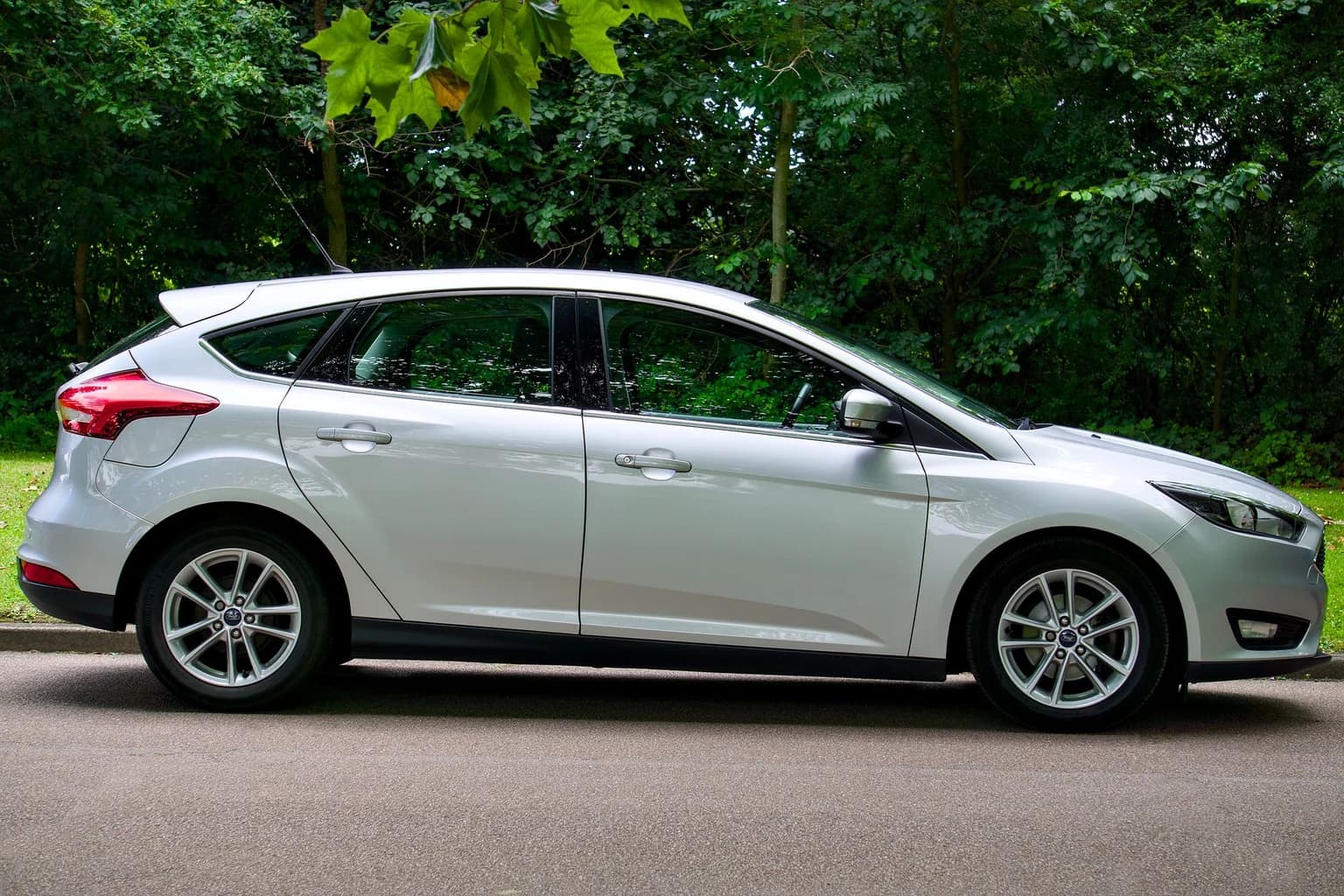 Side view of a stylish white hatchback car parked on a sunny street, surrounded by lush greenery.