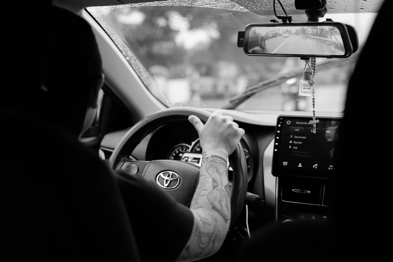 Monochrome image featuring a driver in a Toyota car interior, showcasing a focused driving experience.